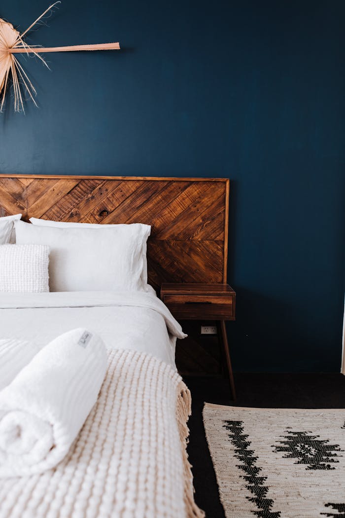 Modern bedroom showcasing dark blue wall, wooden headboard, and minimalist design.